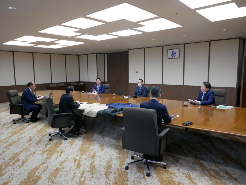 福岡県庁にて、服部知事にサステナブル医療ウェア「sukui」とブロックチェーン技術を活用したDPPシステムについて説明する長谷川社長と正田社長。